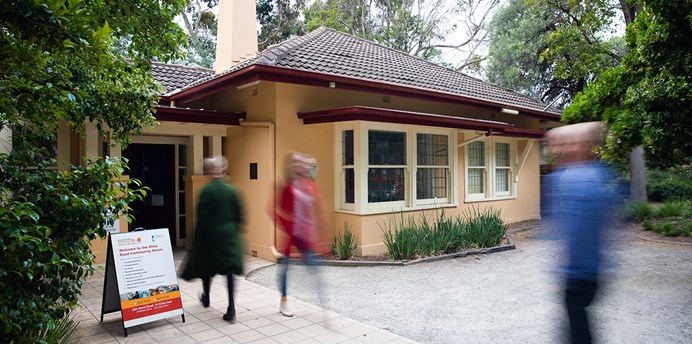Image of the front exterior of a community centre as people walk into and out of the building.