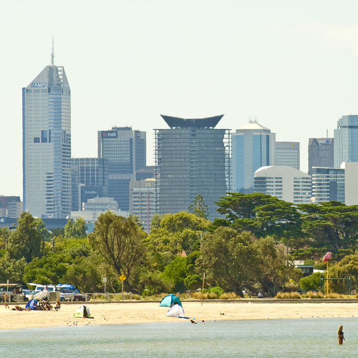 People in the water and enjoying Sandridge Beach with the City skyline in the distance