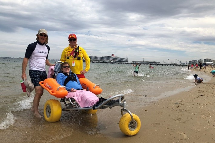 Person with a disability in a beach wheelchair accompanied by life saver
