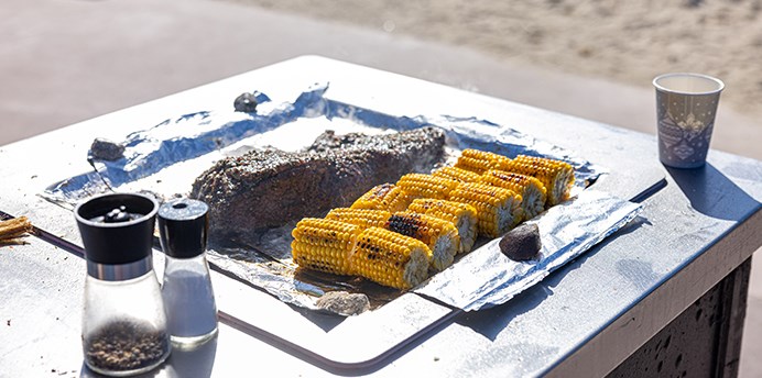 Electric BBQ in a park near the beach with corn cobs and meat cooking on the hot plate